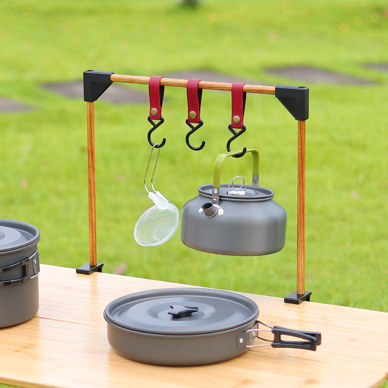 Camping cookware set with pots, pans, and a kettle on a stand outdoors.