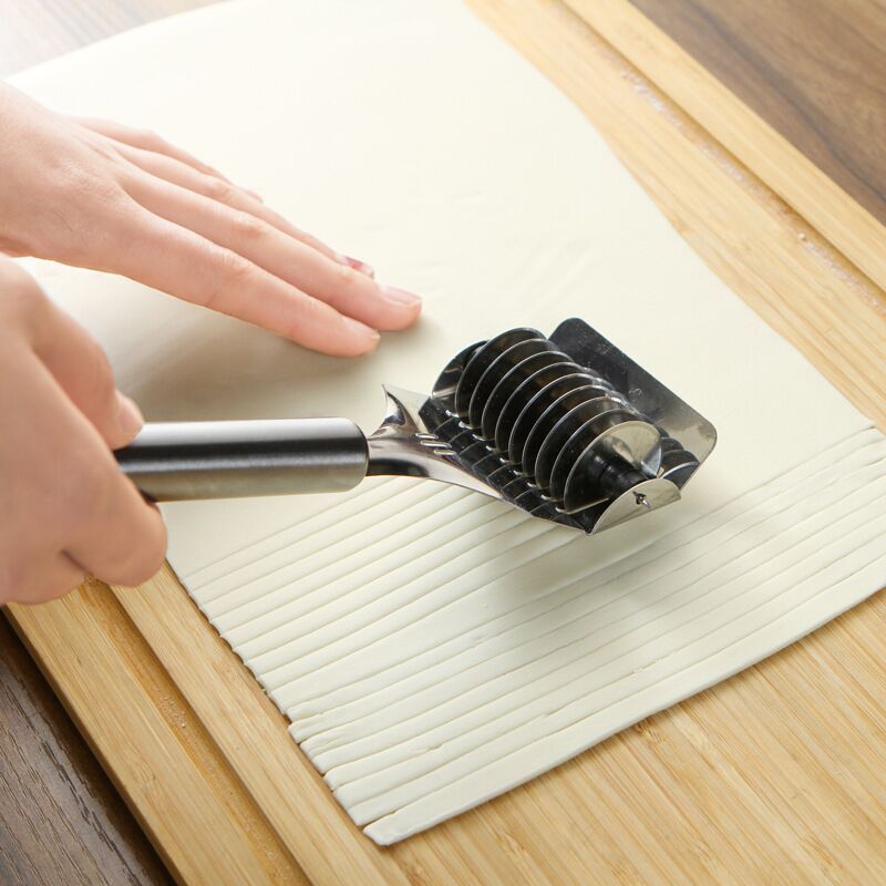 Metallic kitchen tool being used on a cutting board with a hand