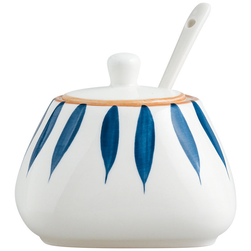 Ceramic sugar bowl with blue leaf patterns and a white spoon on a white background