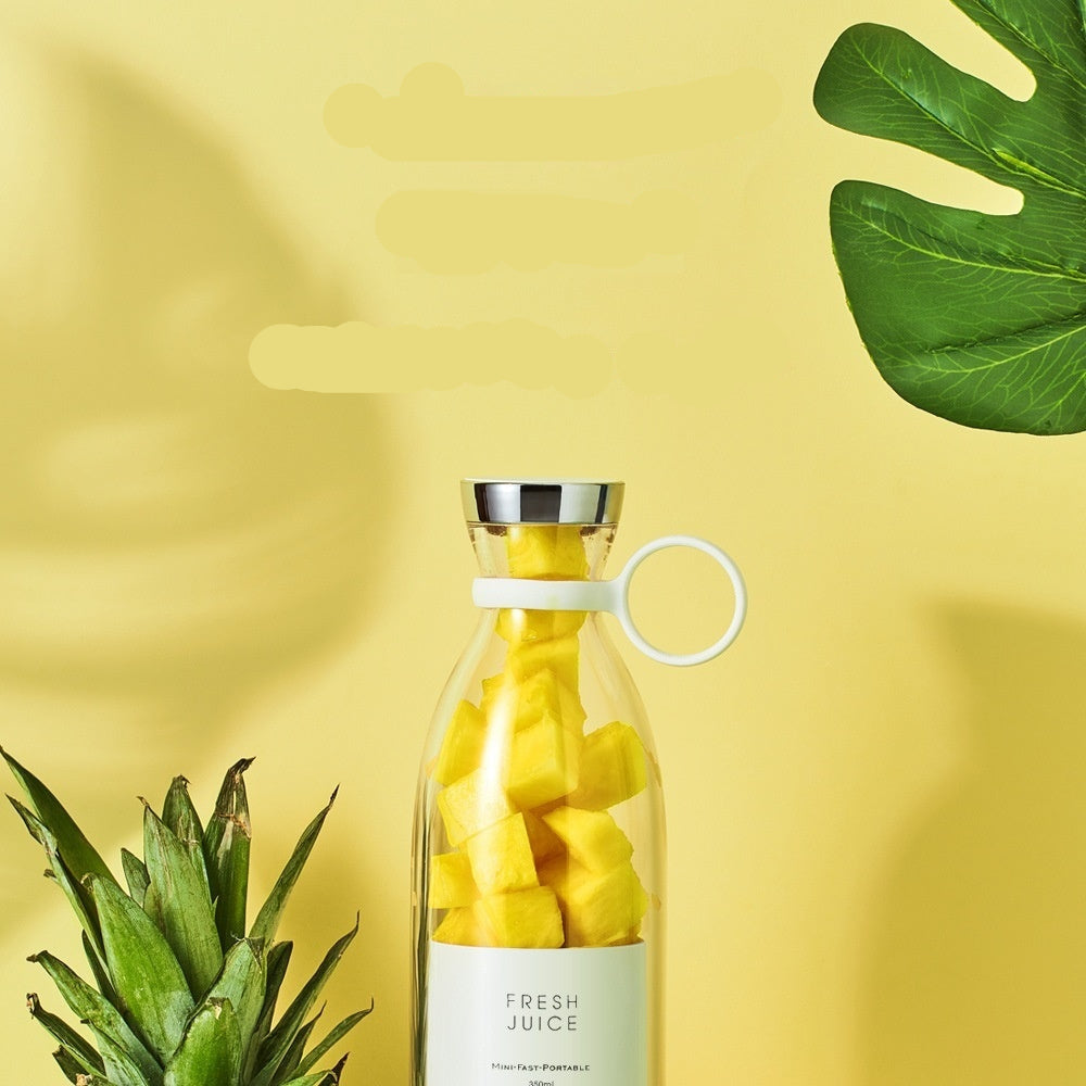 Portable electric juicing cup with pineapple pieces on a yellow background with green leaves.