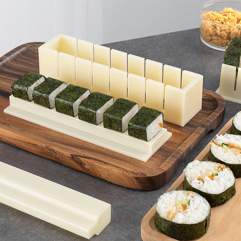 Sushi-making tool on a wooden board with sushi rolls and ingredients.