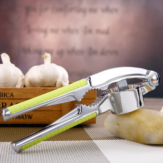 Garlic press with green handle on a wooden surface with garlic bulbs in the background.