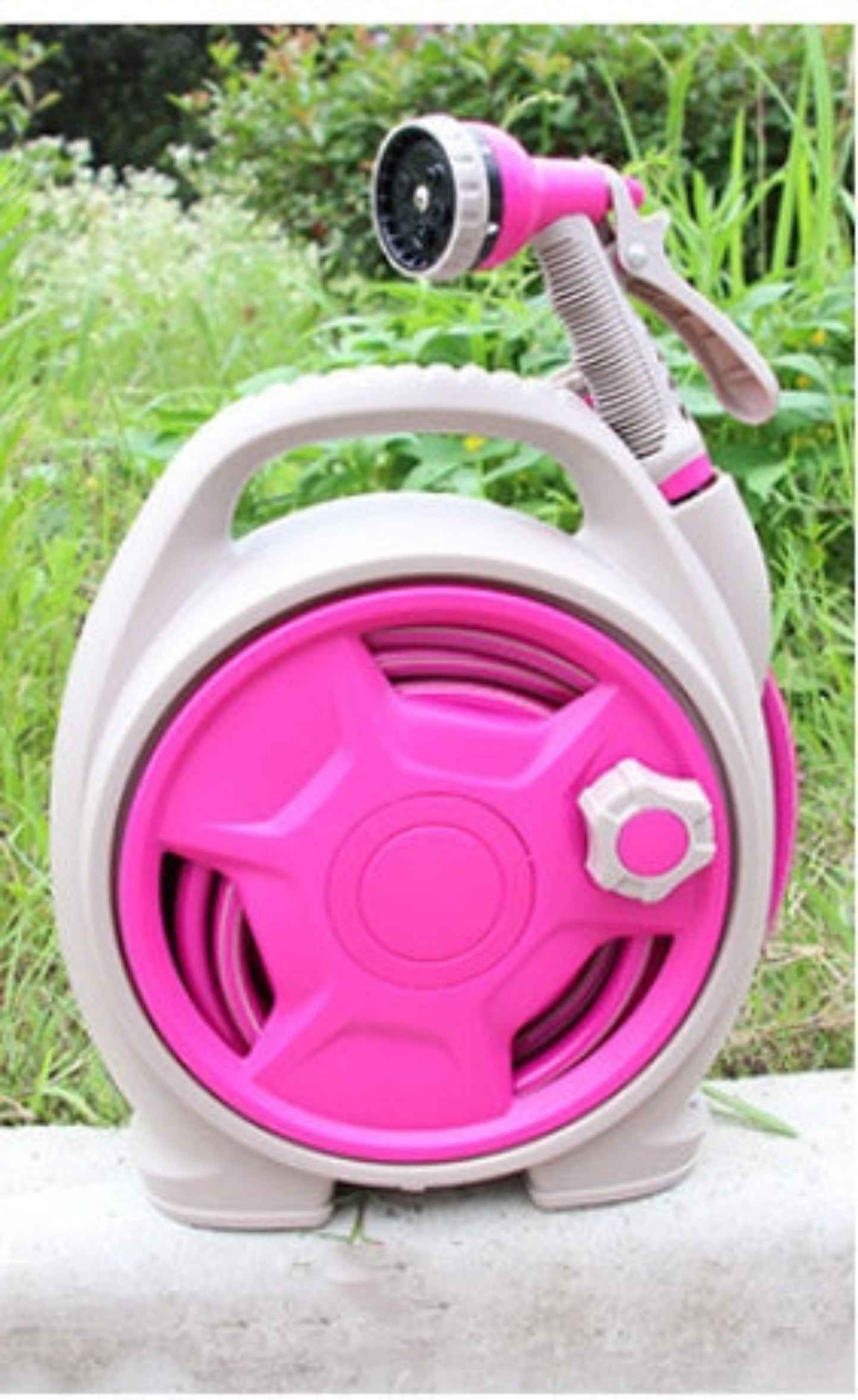 Pink and white garden hose reel with nozzle on a grassy background