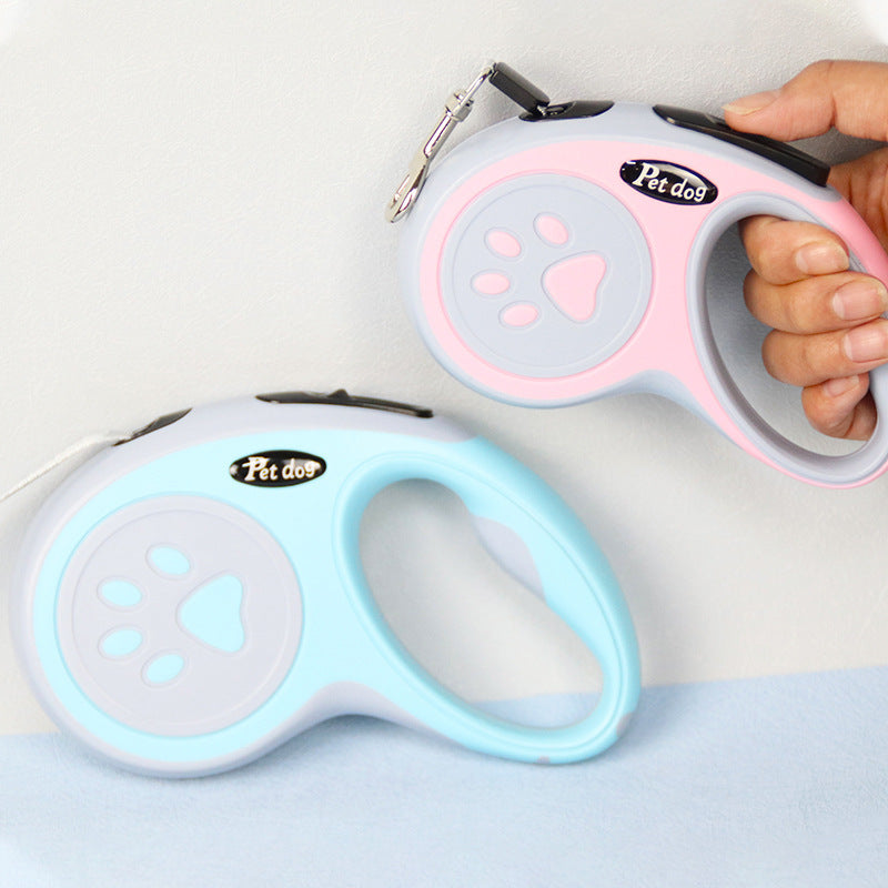 Two retractable dog leashes, one pink and one blue, held by a hand on a light background.