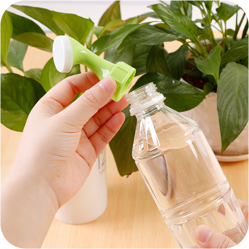 Hand holding a green plant sprayer over a clear bottle with water, against a background of green plants.