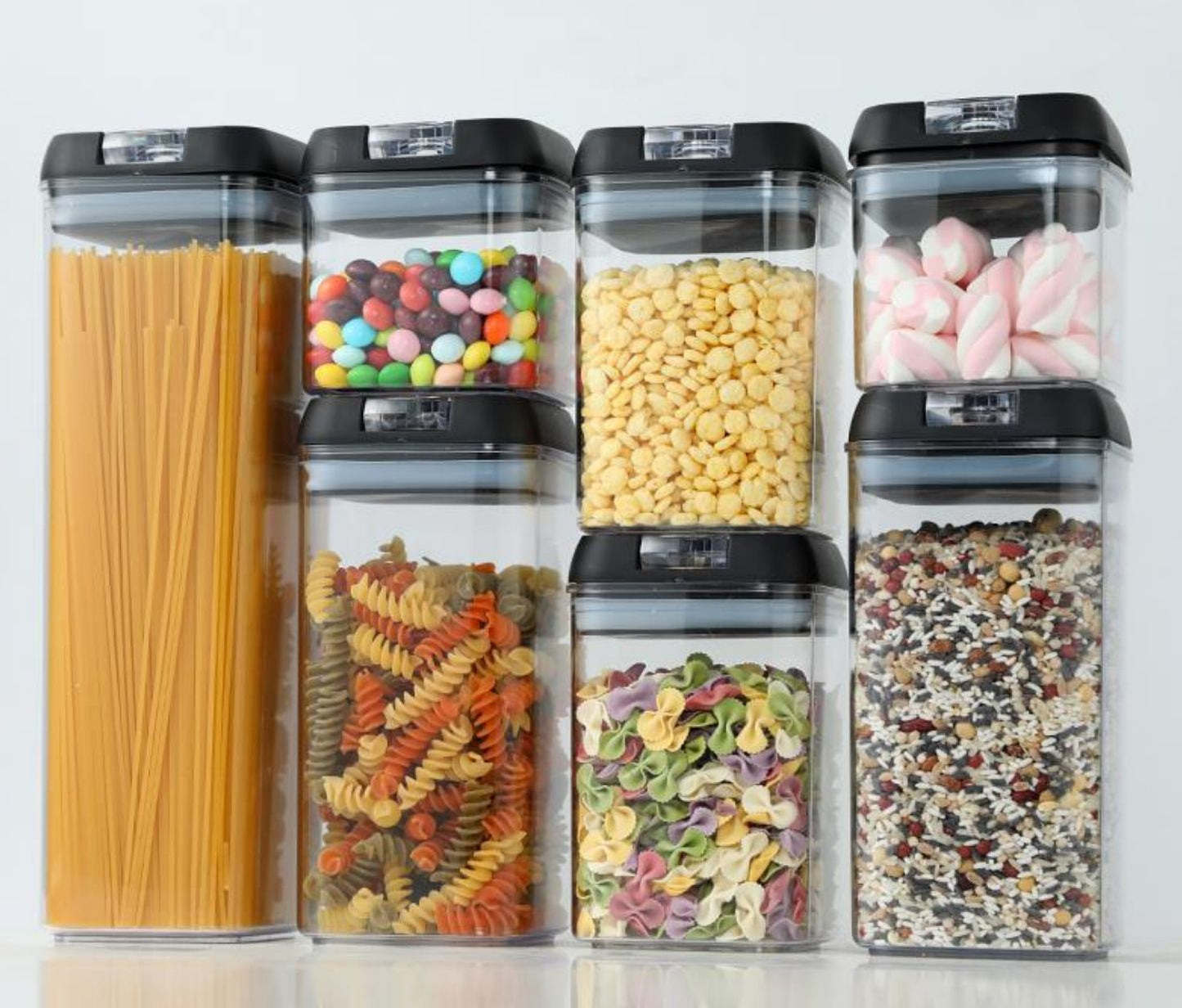 Set of six transparent storage containers with black lids, each filled with different types of pasta and snacks.