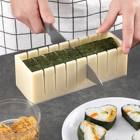 Sushi-making tool with nori sheets and rice being cut into pieces on a gray surface.