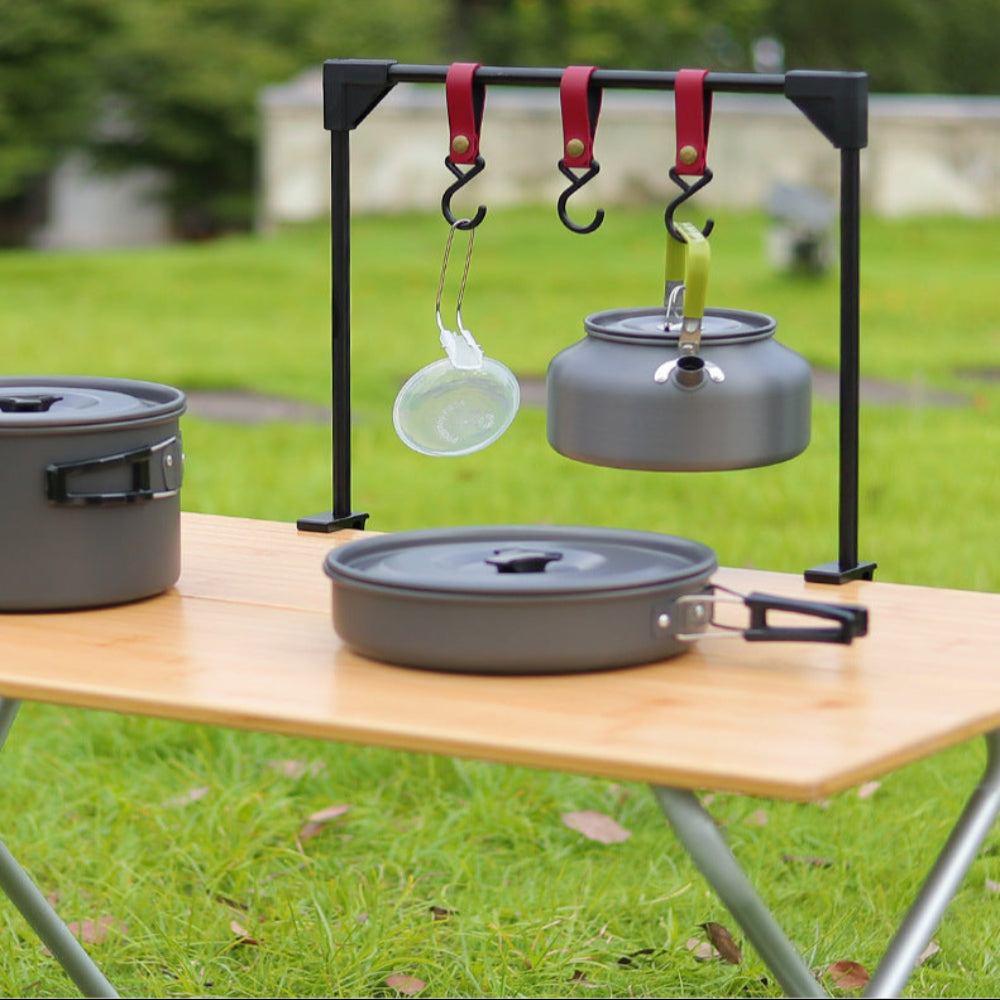 Rack with hooks holding camping pots on a grassy outdoor background