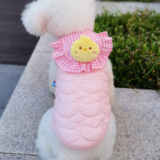 Small dog wearing a pink quilted coat with a chick design on a stone surface.