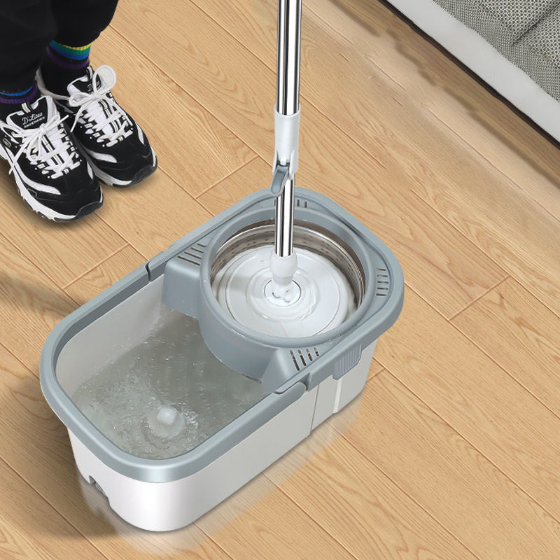 Mop bucket with a mop on a wooden floor, person wearing sneakers in the background.