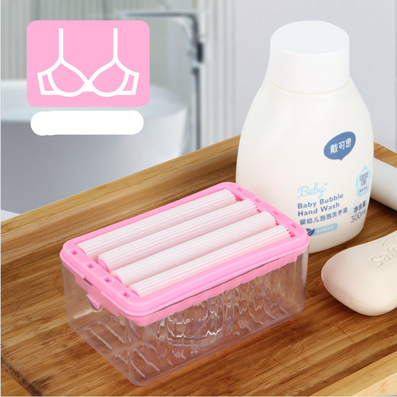 Pink and clear container with rolled-up items on a wooden surface next to a bottle of baby hand wash.