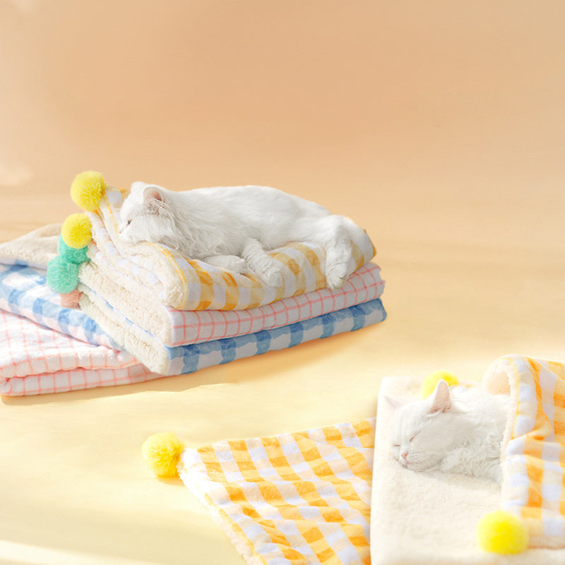 Stack of colorful folded towels with pom-pom accents on a yellow background, featuring a cat interacting with one of the towels.
