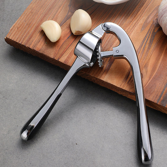 Metal garlic press on a wooden cutting board with garlic cloves