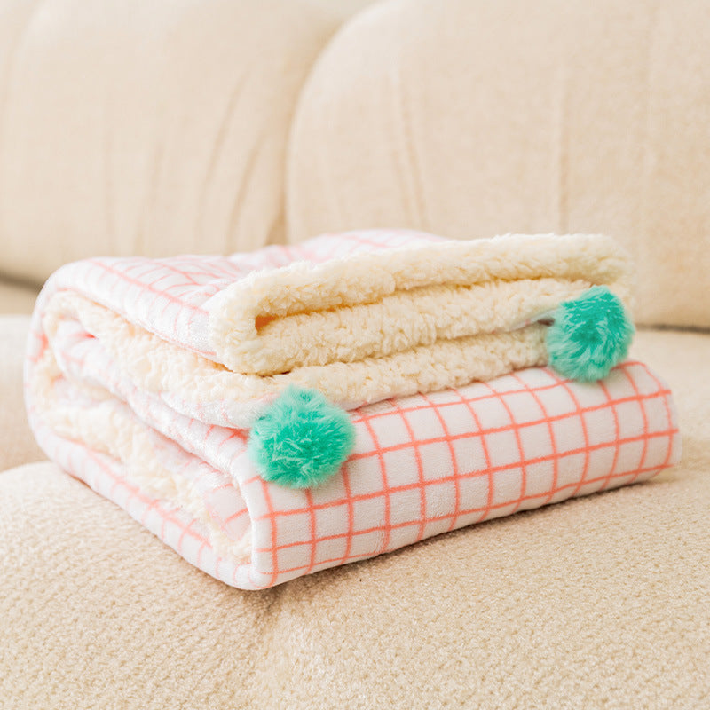 Folded blanket with pom-pom accents on a beige couch