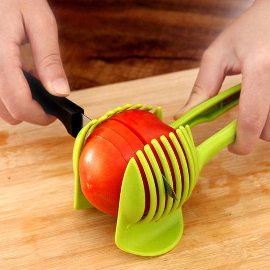 Person using a green tomato slicer to cut a red tomato on a wooden cutting board.