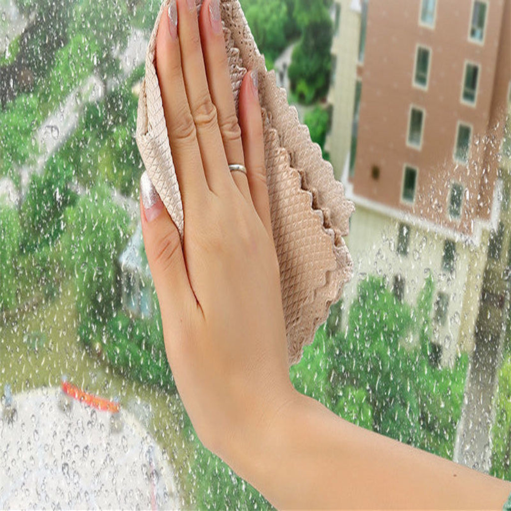 Hand using a microfiber cloth to clean a window with a blurred outdoor view in the background.