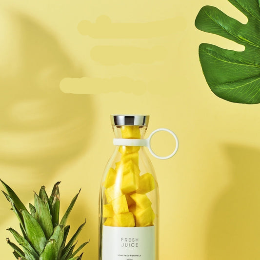 Portable electric juicing cup with pineapple pieces on a yellow background with green leaves.