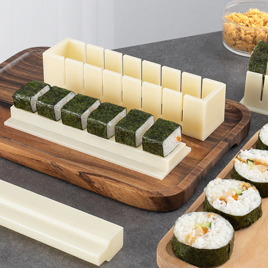 Sushi-making tool on a wooden board with sushi rolls and ingredients.