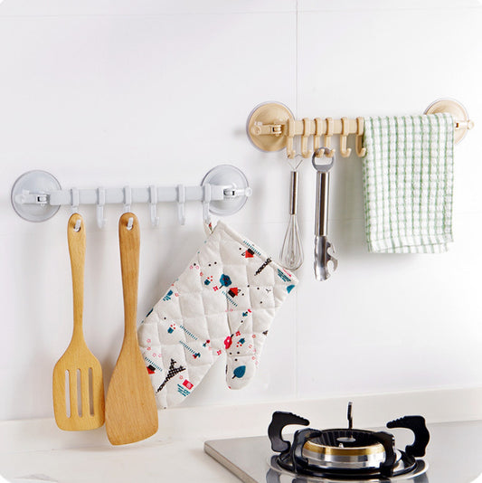 Wall-mounted hooks with kitchen utensils and towels on a white wall.