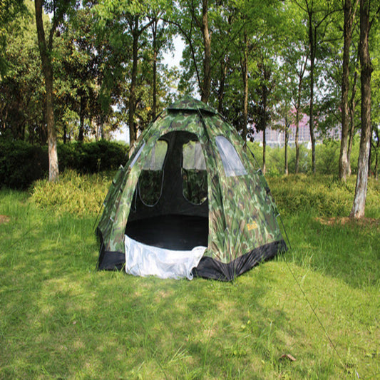 Camouflage tent set up in a grassy area with trees in the background 