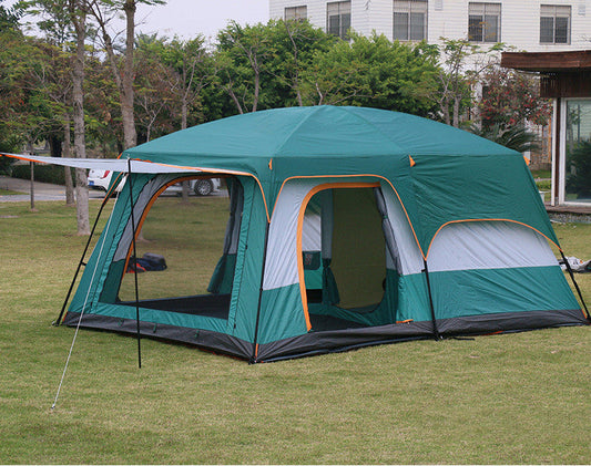 Green camping tent with attached side room on grass, building in background