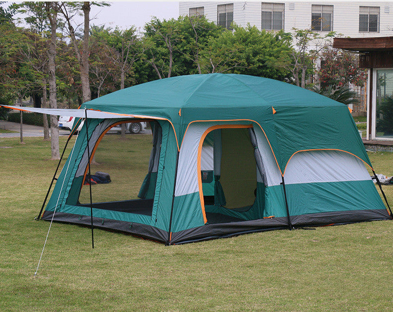 Green camping tent with attached side room on grass, building in background