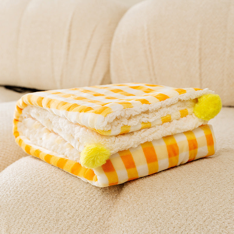 Yellow and white striped blanket with pom-poms on a beige couch