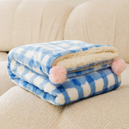Blue and white checkered blanket with pink pom-poms on a beige couch