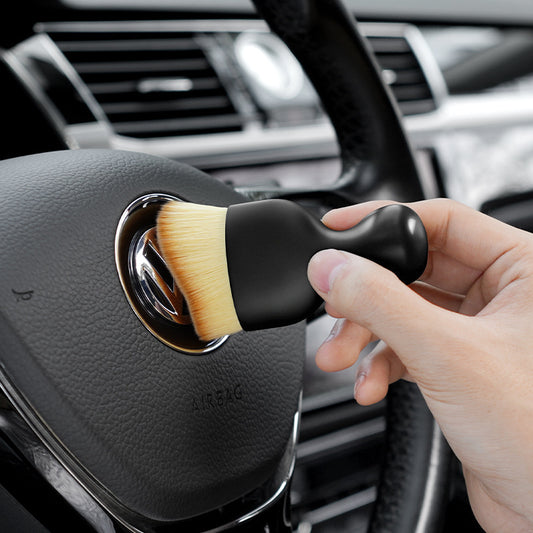 Hand using a car detailing brush to clean a car's air vent.