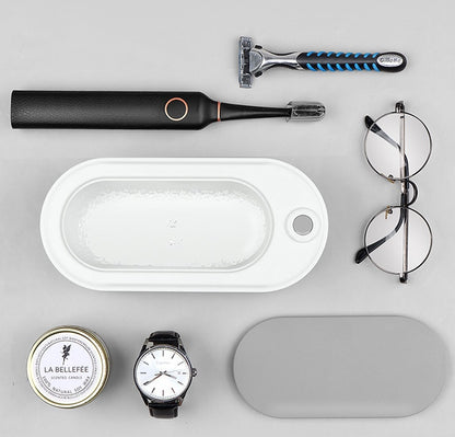 Collection of grooming and personal care items including a razor, electric shaver, glasses, and a watch on a gray background.