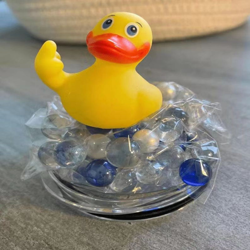 Yellow rubber duck with a red beak and feet, sitting on a clear container filled with blue and clear marbles.