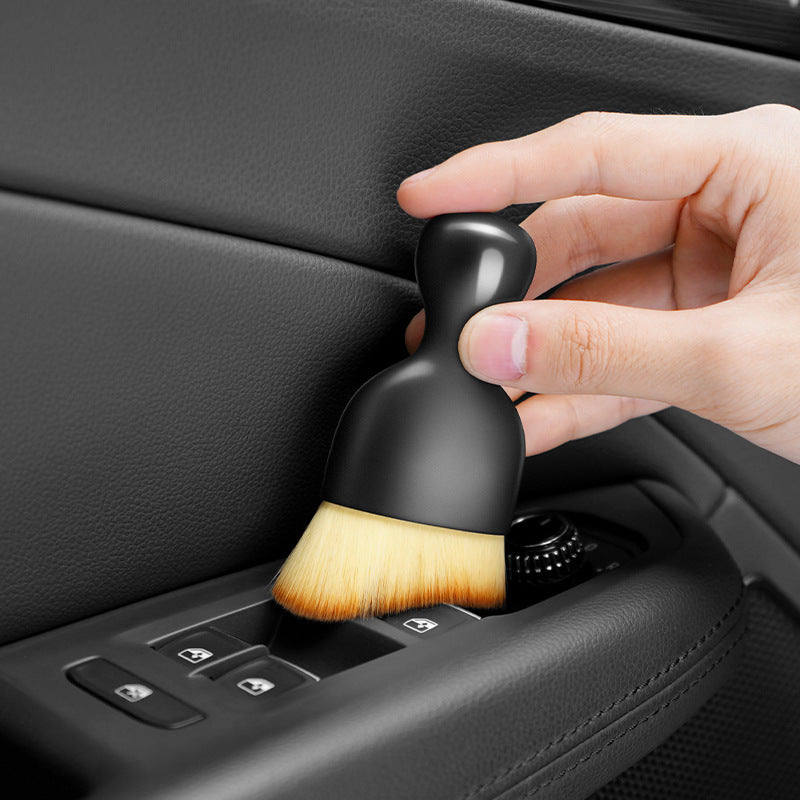 Hand using a car cleaning brush to clean a car's interior panel.