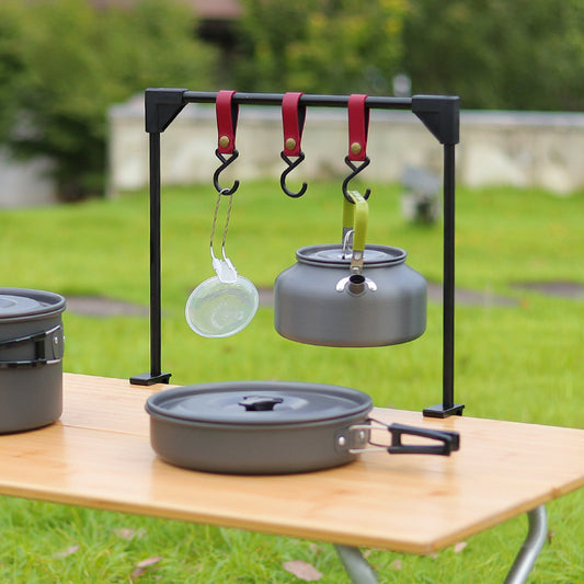 Camping cookware set with pots and pans on a stand outdoors.