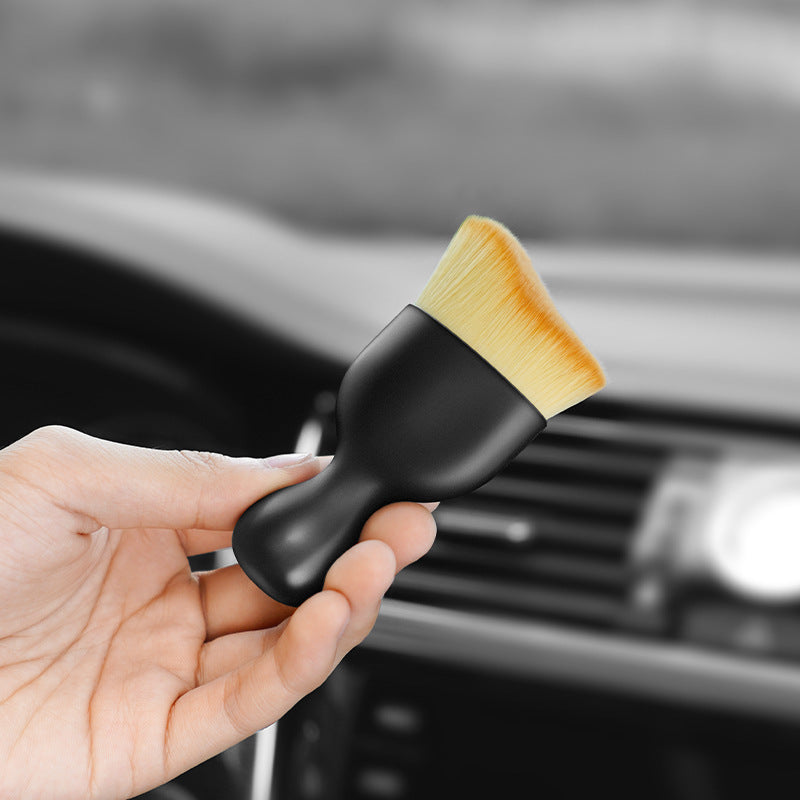 Hand holding a black car detailing brush with a blurred car interior background
