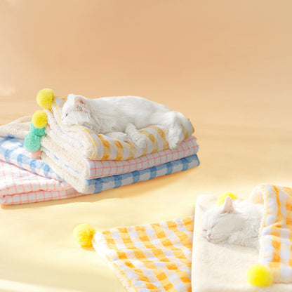 Stack of colorful folded towels with pom-pom accents on a yellow background, featuring a cat interacting with one of the towels.